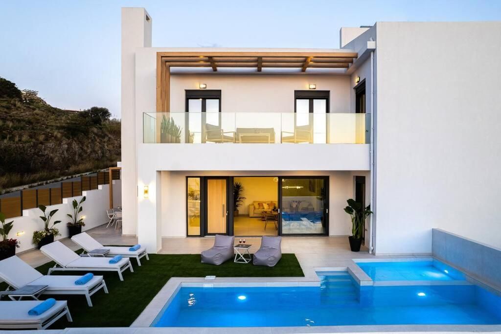 The completed two-storey house at dusk, with the pergola, the glass balcony and the pool in the garden.