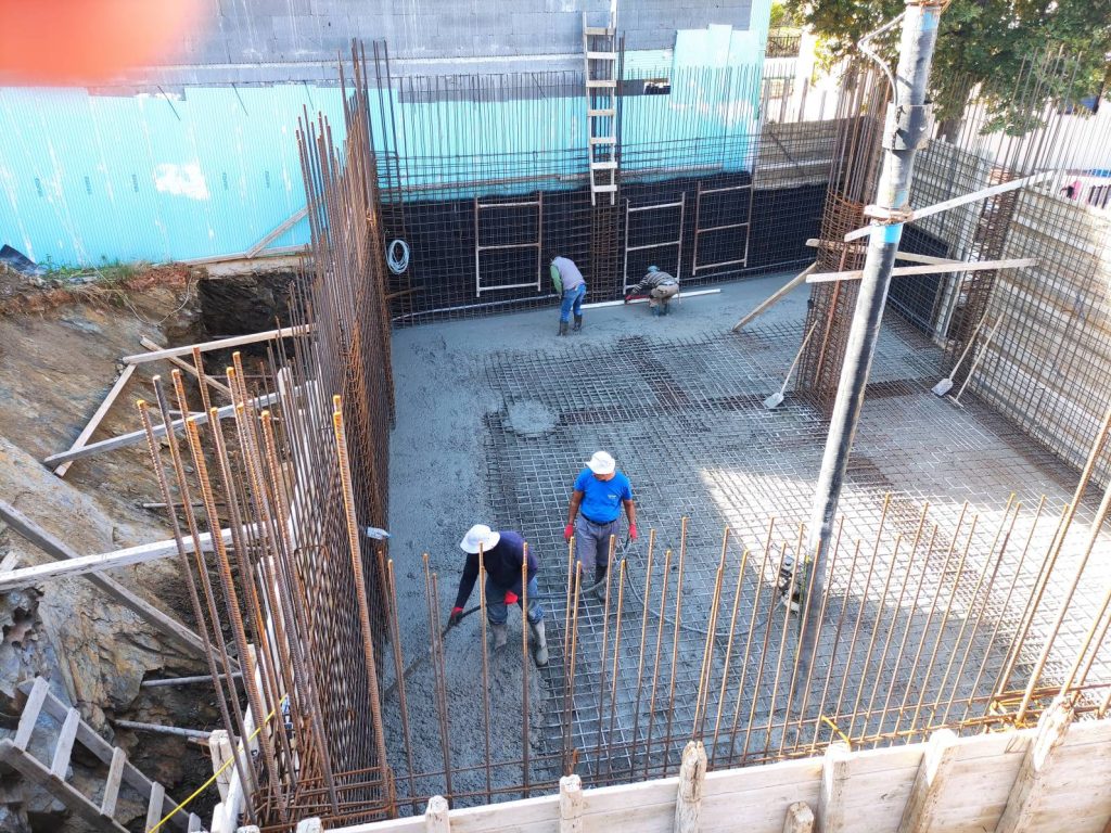 A crew pouring the raft foundation, with the wall starter bars around it.