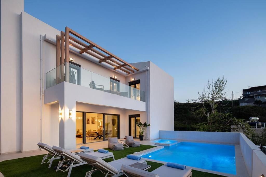 Side view of the house, with sun loungers on the lawn and the pool beside the living room's large glazing.