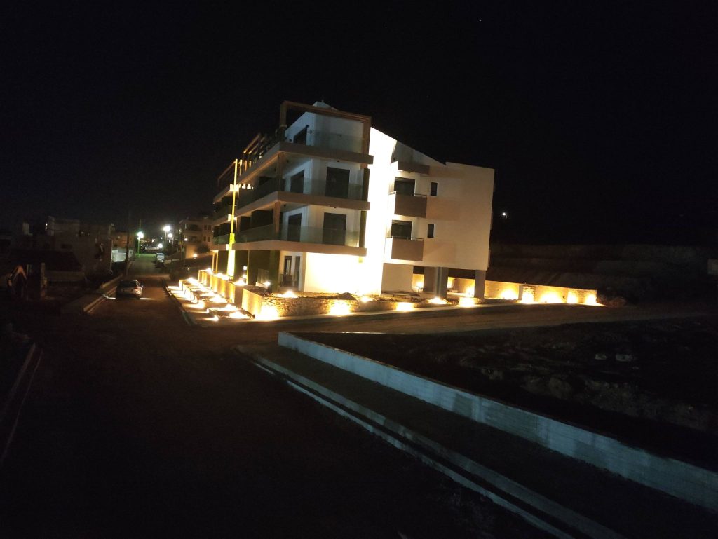 The building at night, with the façades and the surrounding grounds lit up.