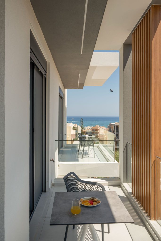 A balcony with a breakfast table, timber louvres and a sea view.