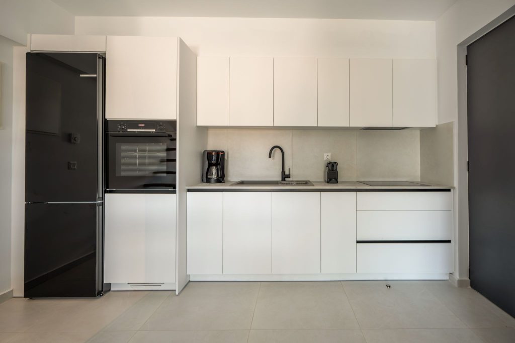 A kitchen with white cabinets, a black fridge and a built-in oven.