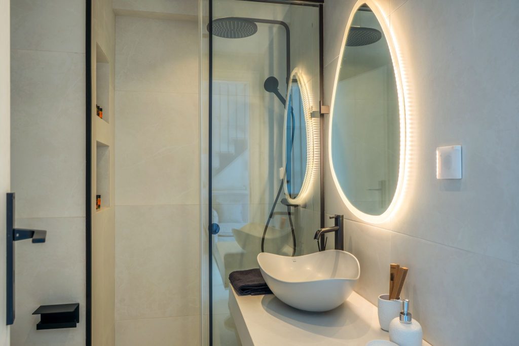 A bathroom with a glass shower, a countertop basin and illuminated mirrors.