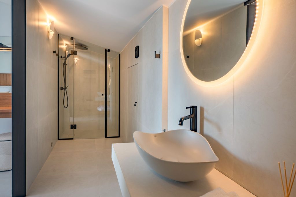 A bathroom with a shower, a countertop basin and a round illuminated mirror.