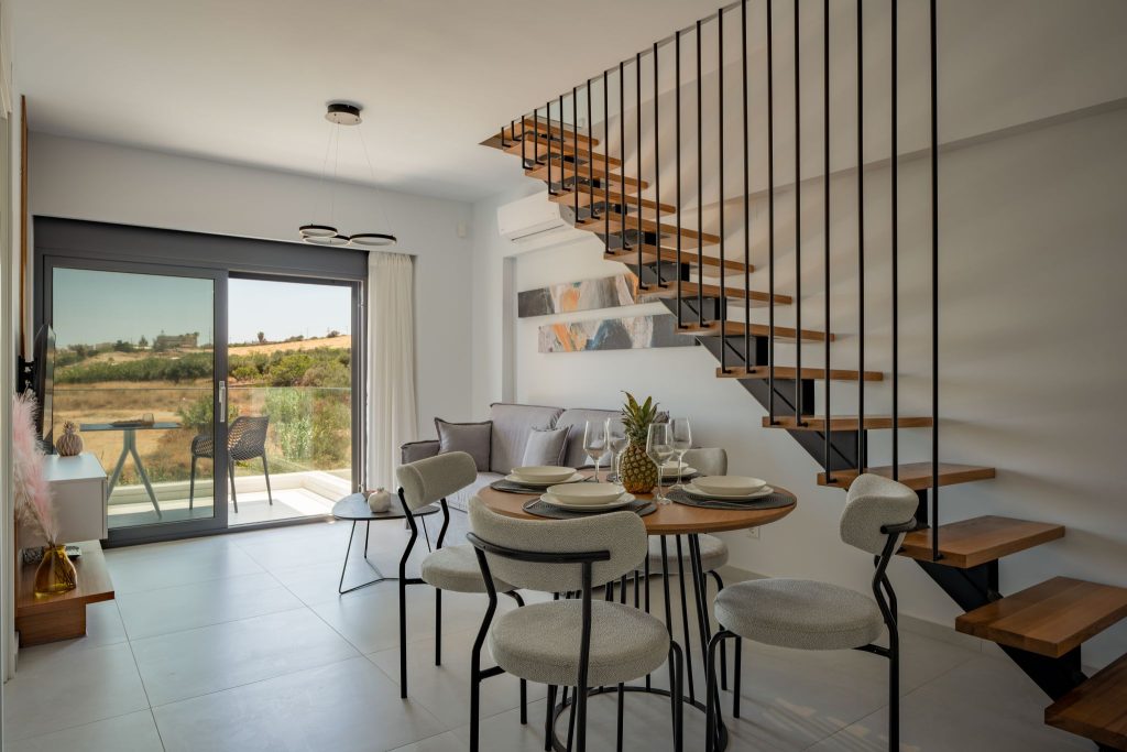A suite's living room with a dining area, a staircase with timber treads and sliding glass doors onto the balcony.