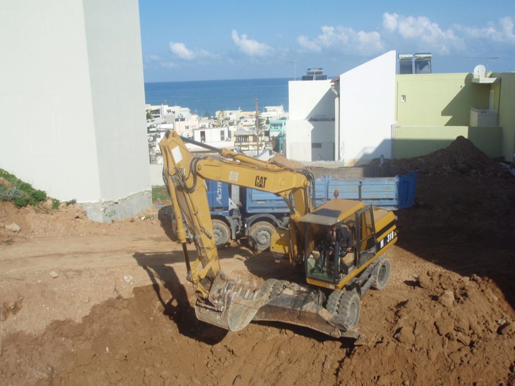 Excavating the plot with an excavator and a truck, with the town and the sea in the background.