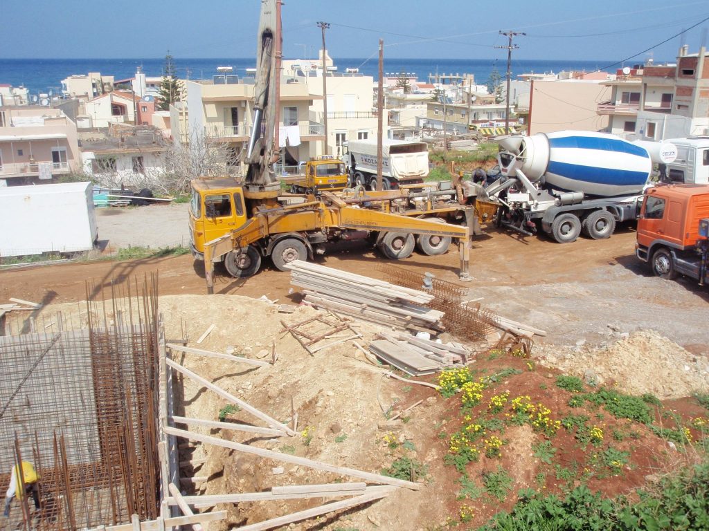 A concrete pump and a mixer truck on the road above the site, with the basement wall reinforcement in the foreground.