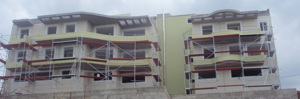The façades behind scaffolding during painting, with the curved balconies in green.