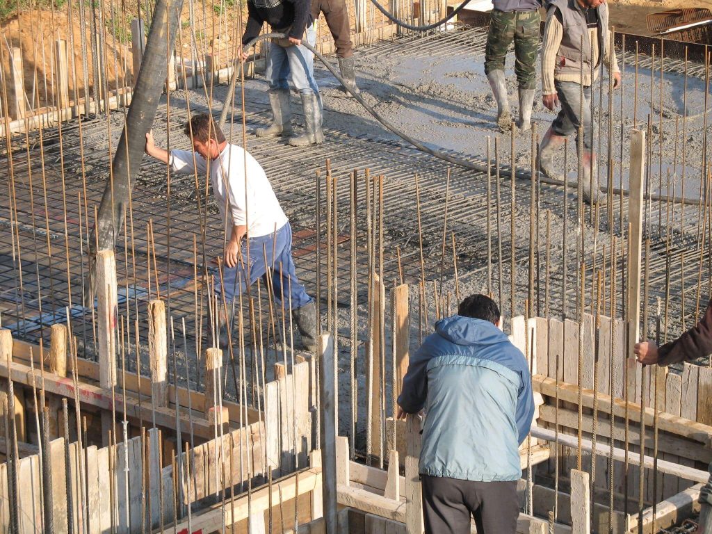 A crew pouring concrete for the slab, standing on the reinforcement.