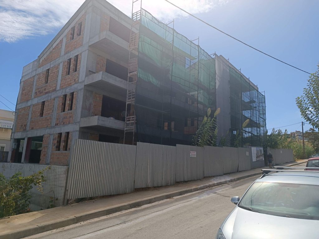 The building with its masonry walls and scaffolding, behind the site fence.