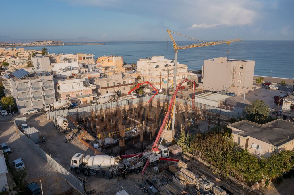 The site from above during a concrete pour, with the crane and the Rethymno beach.