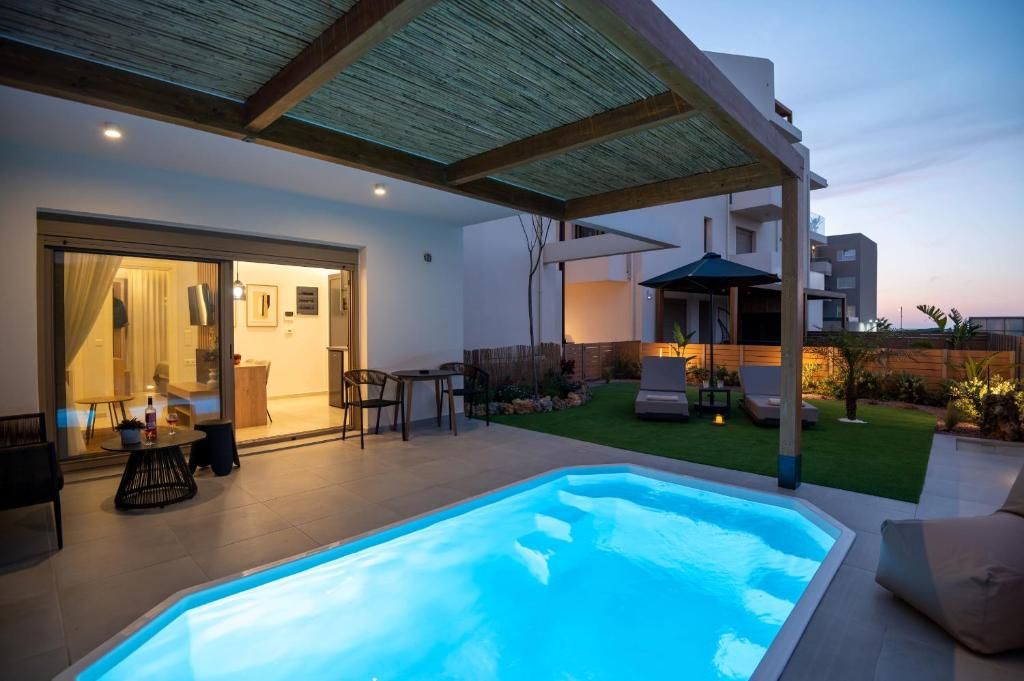 The pool and pergola in front of the living room of a ground-floor apartment, at dusk.