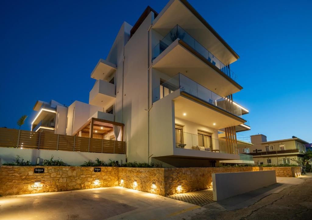 The completed complex at dusk, with glass-railed balconies and the lit stonework at the base.