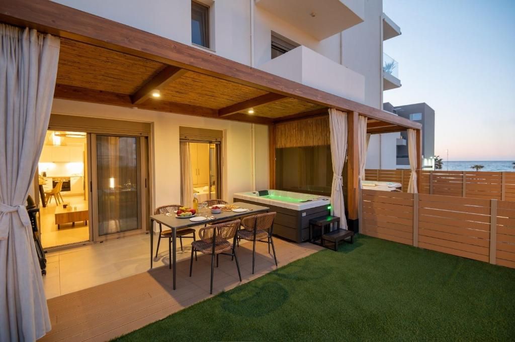 A covered veranda with a dining table and a hot tub, in an apartment's garden with a sea view.