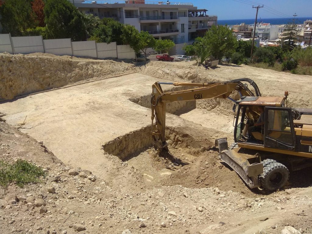 Excavating the plot with an excavator, with the town and the sea in the background.